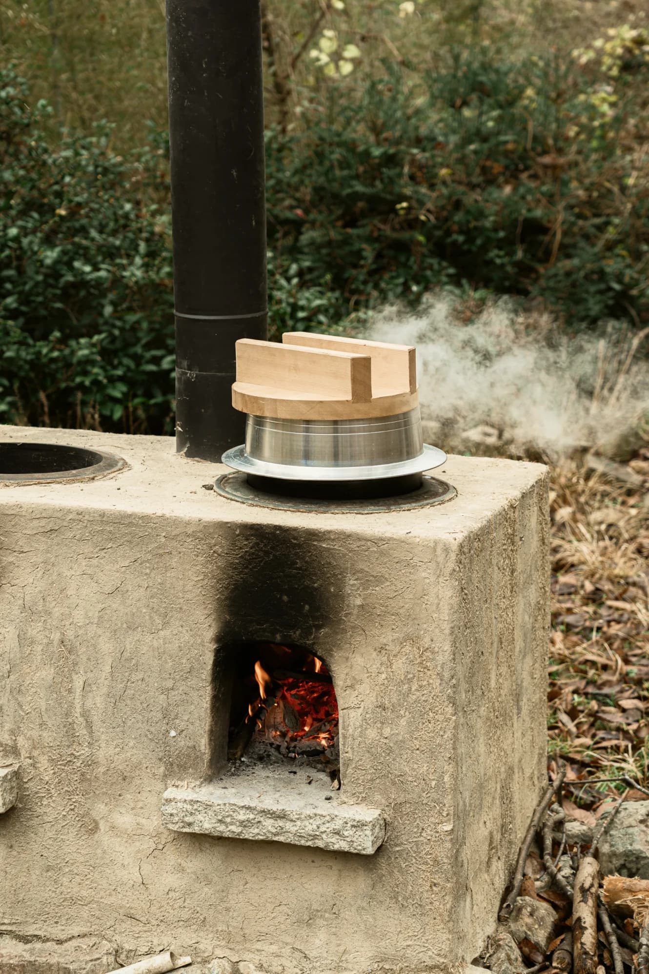 Rustic outdoor stove with fire and traditional Japanese rice cooker emitting steam