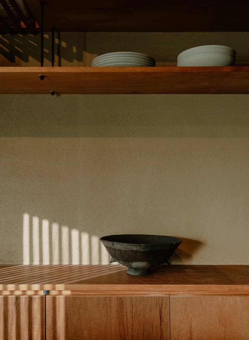 Ceramic bowl and plates on wooden kitchen shelves in sunlight