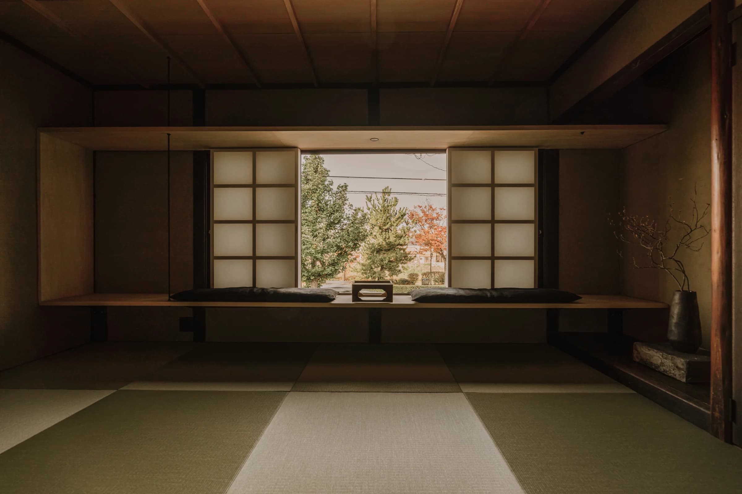 Tatami room with open shoji screens framing autumn foliage through a wide window